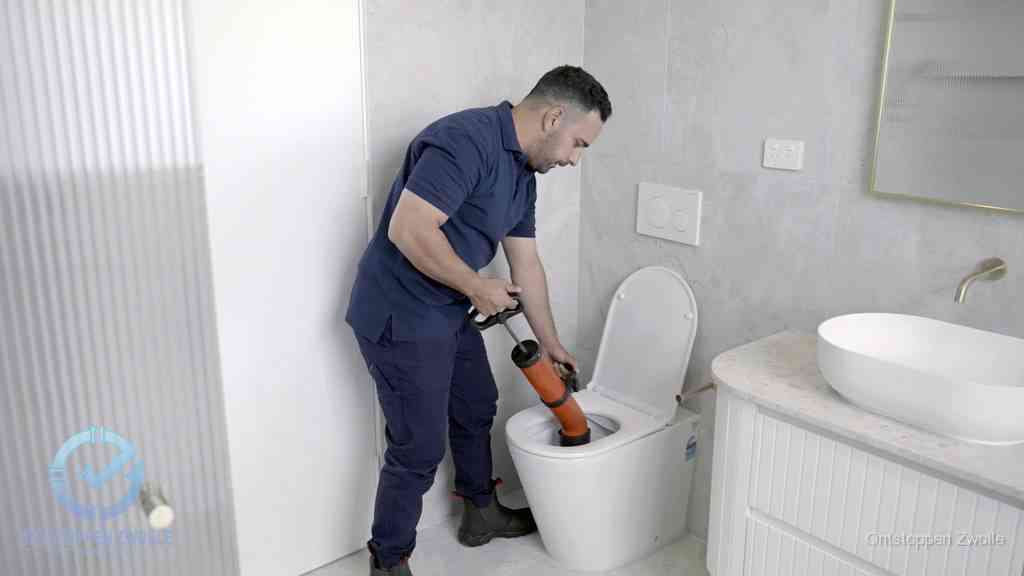 Een monteur buigt over een wandcloset en duwt met de hand een persluchtontstopper in de toiletpot om de verstopping handmatig los te maken in Zwolle