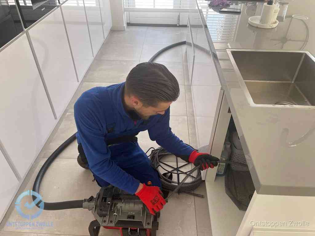 Een monteur ontstopt de keukenafvoer onder de spoelbak met een elektrische veermachine in Zwolle