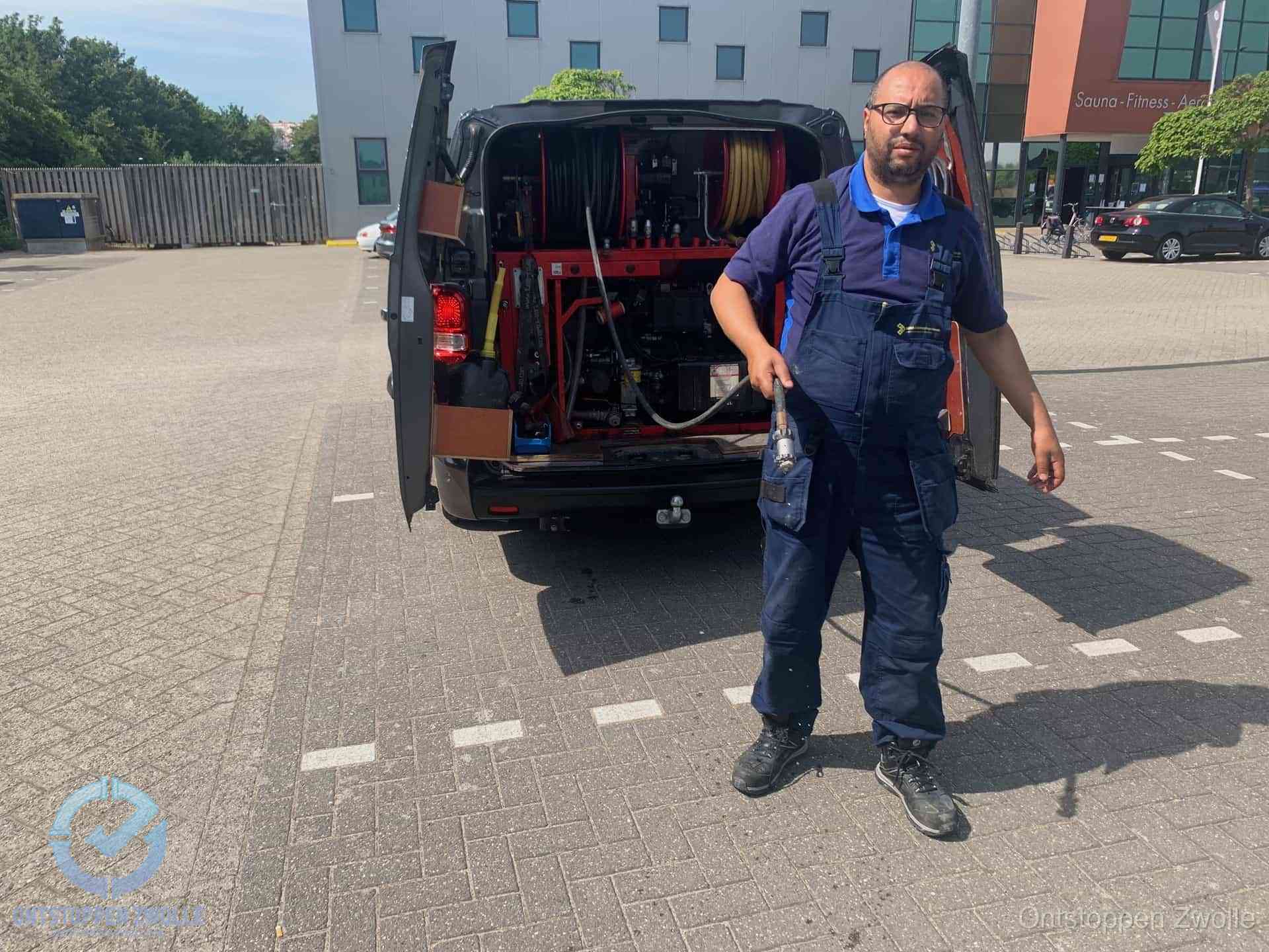 Een monteur bij zijn bestelbus met een hogedruk- en rioolreinigingsunit, klaar om de oorzaak van terugkerende wc-verstoppingen aan te pakken in Zwolle