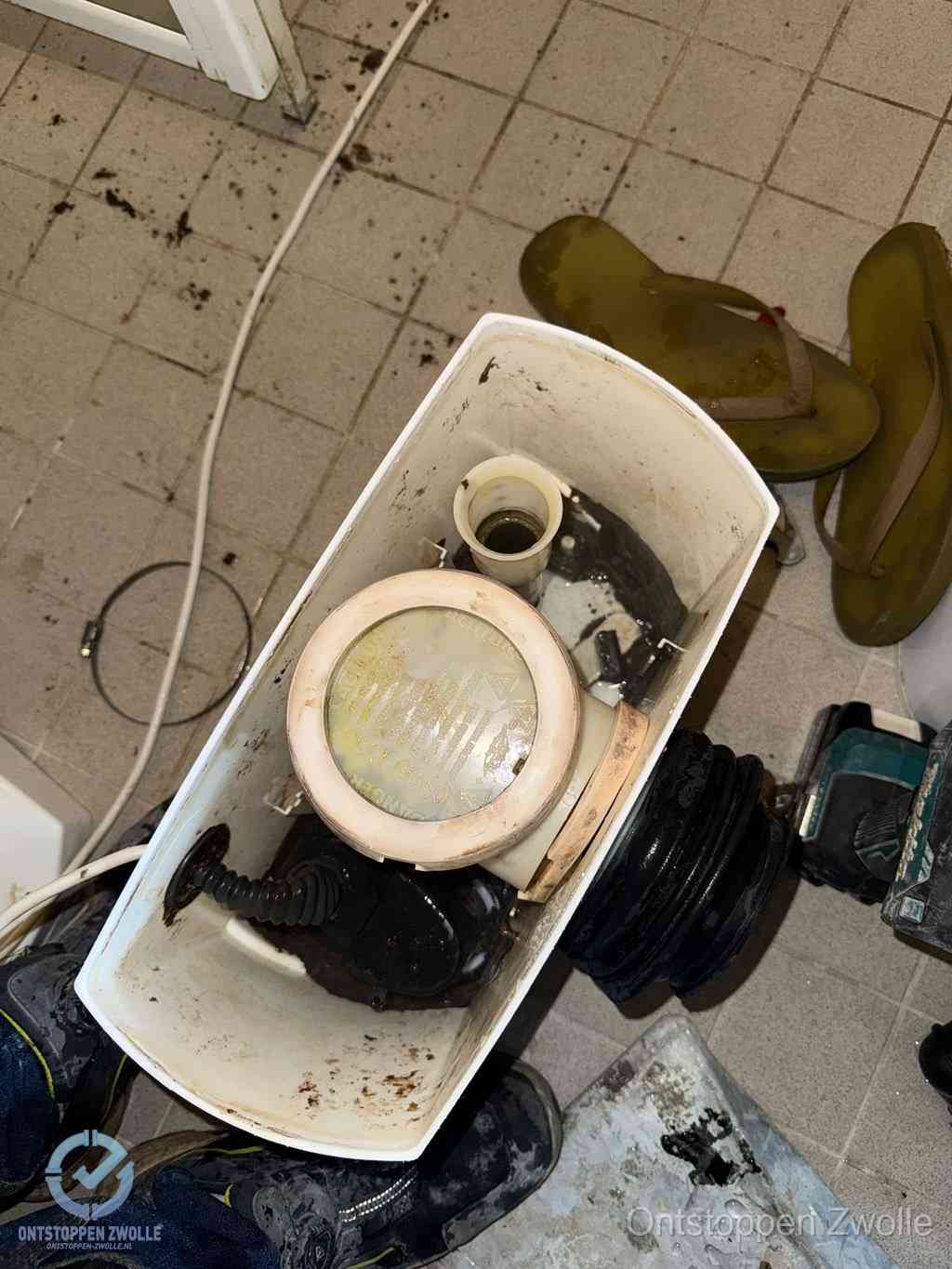 Een gedemonteerde toiletpot op de vloer met ontstoppingsveer en gereedschap ernaast, het verwijderen van een vastzittend voorwerp uit de wc in Zwolle