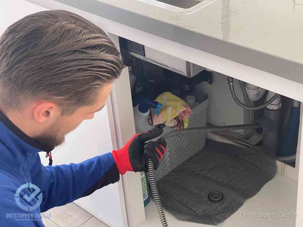 Een monteur voert een flexibele ontstoppingsveer in de afvoer om een verstopping voorbij de bocht van het toilet te bereiken in Zwolle