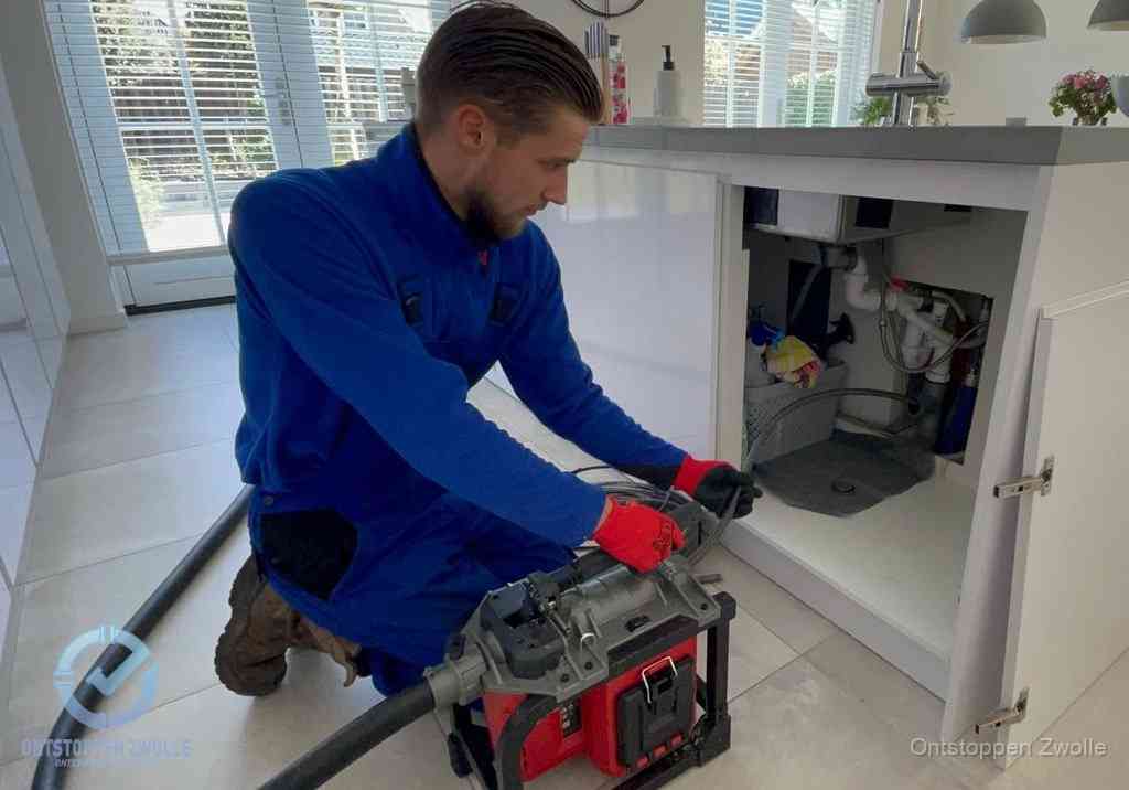 Een monteur voert een professionele elektrische ontstoppingsmachine in de afvoer onder de spoelbak tijdens het gootsteen ontstoppen in Zwolle